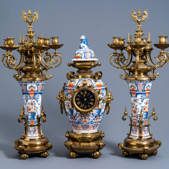 A large French brass mounted three-piece polychrome decorated earthenware clock garniture with floral design, 19th/20th C.