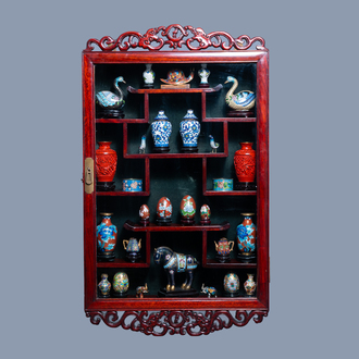 A varied collection of Chinese cloisonné and cinnabar lacquer items in a display cabinet, 20th C.